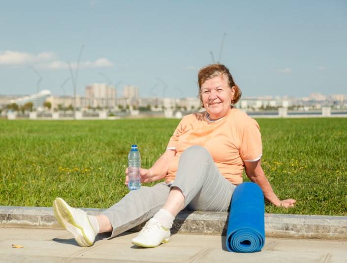 elderly woman resting and drinking water while exercising outside